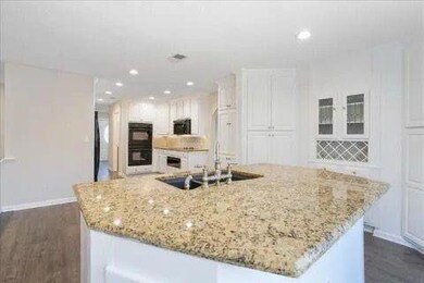 Kitchen with dobule oven black, a sink, baseboards, white cabinetry, and dark wood-style floors
