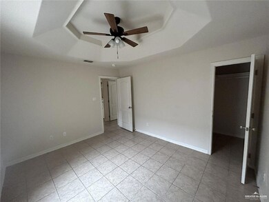 Unfurnished bedroom with a tray ceiling, a spacious closet, light tile patterned floors, a ceiling fan, and a closet