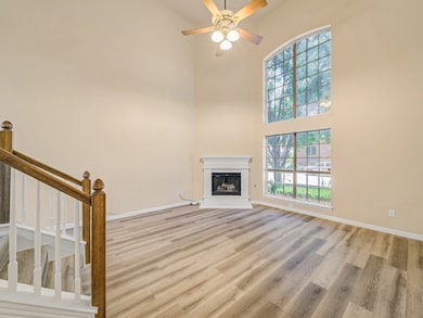 Unfurnished living room with light wood-style floors, a fireplace with raised hearth, ceiling fan, and a high ceiling
