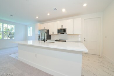 Kitchen with an island with sink, stainless steel appliances, light tile flooring, and white cabinetry