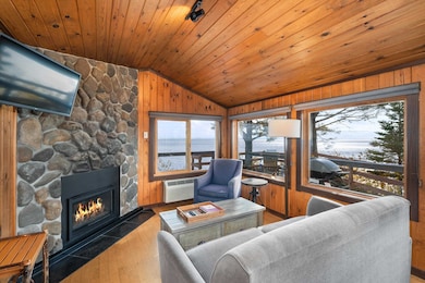 Living area featuring vaulted ceiling, a stone fireplace, hardwood / wood-style floors, a water view, and wooden walls