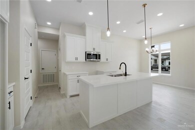 Kitchen featuring a sink, stainless steel microwave, light wood-style floors, white cabinetry, and recessed lighting