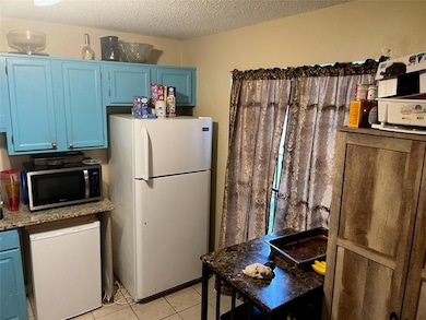 Kitchen featuring freestanding refrigerator, stainless steel microwave, blue cabinetry, refrigerator, and a textured ceiling