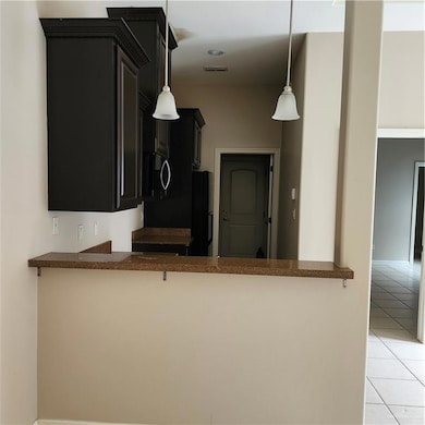 Kitchen with dark cabinetry, light tile patterned flooring, refrigerator, decorative light fixtures, and a peninsula