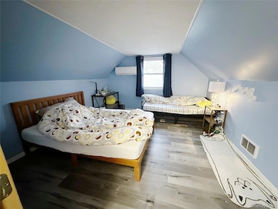 Bedroom featuring vaulted ceiling, wood finished floors, and an AC wall unit