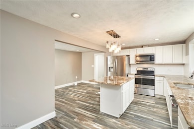 Kitchen with white cabinetry, a center island, stainless steel appliances, recessed lighting, and decorative light fixtures
