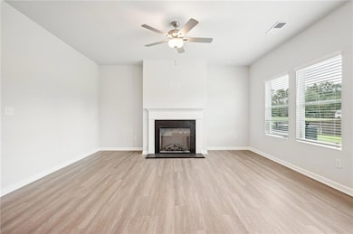 Unfurnished living room featuring a ceiling fan, wood finished floors, and a fireplace with raised hearth