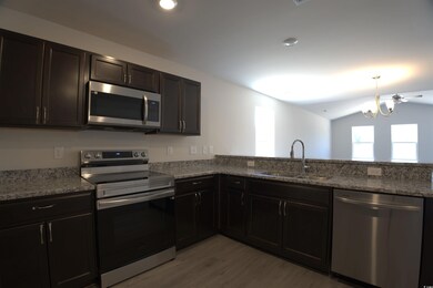 Kitchen featuring stainless steel appliances, light wood finished floors, light stone countertops, lofted ceiling, and a chandelier
