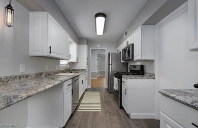 Kitchen featuring light hardwood flooring, appliances with stainless steel finishes, light stone counters, and white cabinetry