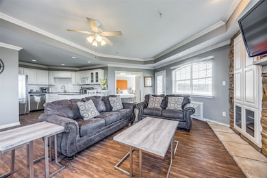 Tiled living room with ceiling fan, ornamental molding, and a tray ceiling
