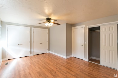 Unfurnished bedroom with multiple closets, light wood finished floors, ceiling fan, and a textured ceiling