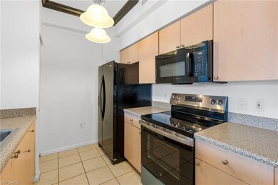 Kitchen featuring stainless steel electric range oven, light countertops, light tile patterned floors, light brown cabinetry, and freestanding refrigerator