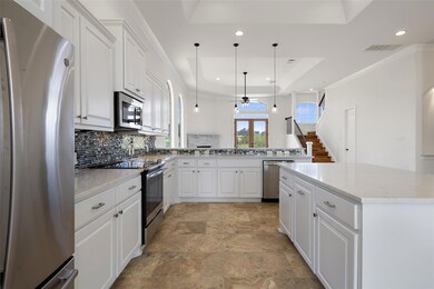Kitchen with stainless steel appliances, white cabinetry, a tray ceiling, hanging light fixtures, and ornamental molding