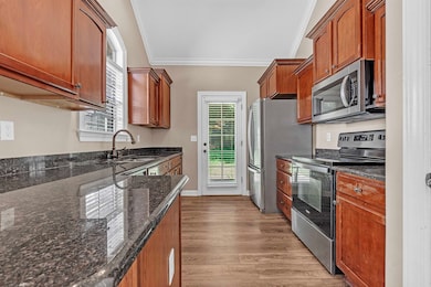 Kitchen featuring stainless steel appliances, ornamental molding, wood finished floors, dark stone counters, and brown cabinetry