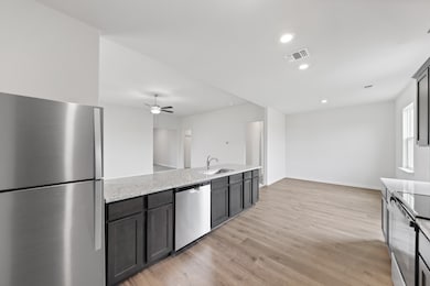 Kitchen with appliances with stainless steel finishes, recessed lighting, light wood finished floors, light stone counters, and ceiling fan