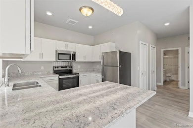 Kitchen with appliances with stainless steel finishes, light stone countertops, white cabinets, a peninsula, and light wood finished floors