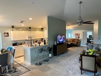 Kitchen with white microwave, a ceiling fan, light colored carpet, a kitchen breakfast bar, and recessed lighting