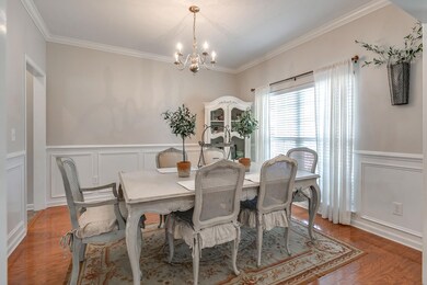 A new light fixture hangs in this Formal Dining Room. The wainscoting & crown molding wrap around the bright Dining Area.