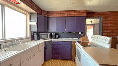 Kitchen with white appliances, light countertops, brick wall, and light flooring