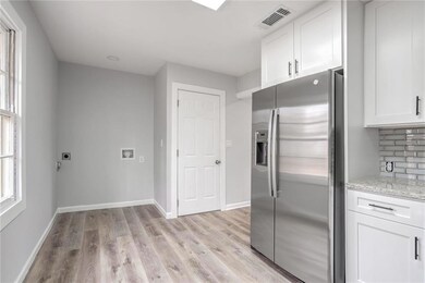 Kitchen featuring stainless steel refrigerator with ice dispenser, light wood-style floors, white cabinets, light stone counters, and baseboards