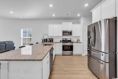 Kitchen with appliances with stainless steel finishes, white cabinetry, light stone countertops, a kitchen breakfast bar, and recessed lighting