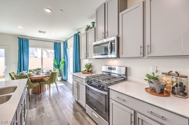 Kitchen featuring stainless steel appliances, light stone countertops, light wood-type flooring, gray cabinetry, and recessed lighting. Photo is representational only; actual home finishes may vary.