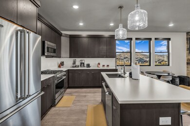 Kitchen with high end appliances, dark brown cabinets, light countertops, light wood finished floors, and a kitchen island with sink