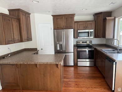Kitchen featuring appliances with stainless steel finishes, a peninsula, a breakfast bar area, dark wood finished floors, and a textured ceiling