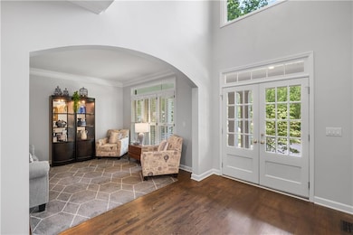 Foyer with arched walkways, french doors, crown molding, wood finished floors, and healthy amount of natural light
