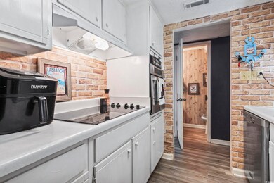 Kitchen featuring black electric cooktop, brick wa