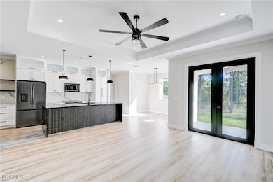 Kitchen with white cabinetry, a tray ceiling, ornamental molding, appliances with stainless steel finishes, and a center island with sink