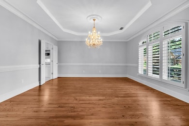 Unfurnished room with a raised ceiling, wood finished floors, a chandelier, and ornamental molding