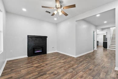 Unfurnished living room with dark wood-style floors, ceiling fan, recessed lighting, stairs, and a glass covered fireplace