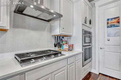 Kitchen featuring wall chimney exhaust hood, white cabinetry, dark wood-type flooring, appliances with stainless steel finishes, and light stone counters