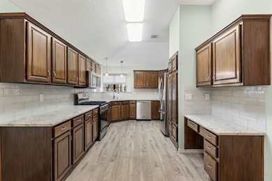 The kitchen welcomes guests with a vaulted ceiling, a bright box window, granite countertops, and a convenient built-in desk area. Ample cabinetry provides generous storage throughout.