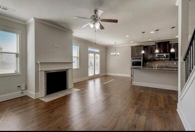 Unfurnished living room featuring a fireplace with flush hearth, dark wood-style floors, visible vents, ceiling fan with notable chandelier, and crown molding