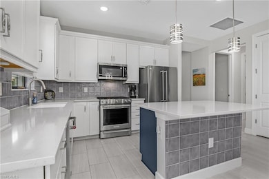 Kitchen with appliances with stainless steel finishes, tasteful backsplash, white cabinets, a center island, and hanging light fixtures