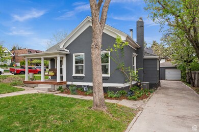 View of front of house with covered porch, a front yard, stucco siding, an outdoor structure, and a chimney