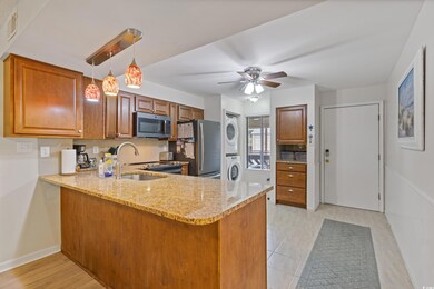 Kitchen featuring brown cabinetry, stacked washer and dryer, a peninsula, light stone counters, and appliances with stainless steel finishes