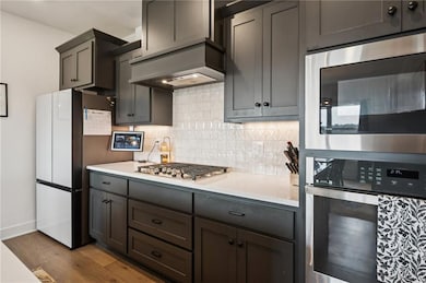 Kitchen with stainless steel appliances, backsplash, engineered hardwood floors, and light stone counters