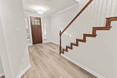 Foyer entrance with ornamental molding, light wood-style flooring, and stairs
