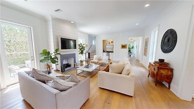 Living room featuring healthy amount of natural light, a large fireplace, light wood-style flooring, ornamental molding, and recessed lighting