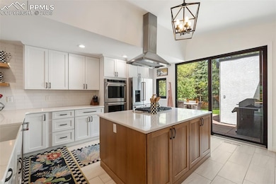 Kitchen with island exhaust hood, appliances with stainless steel finishes, decorative backsplash, light countertops, and white cabinetry