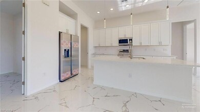 Kitchen featuring stainless steel appliances, light marble finish flooring, baseboards, white cabinets, and a sink
