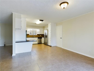 Kitchen with dark countertops, crown molding, decorative backsplash, a textured ceiling, and stainless steel appliances