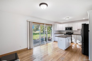 Kitchen with backsplash, appliances with stainless steel finishes, white cabinetry, and light wood-type flooring