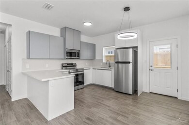 Kitchen featuring appliances with stainless steel finishes, light countertops, gray cabinets, hanging light fixtures, and a peninsula