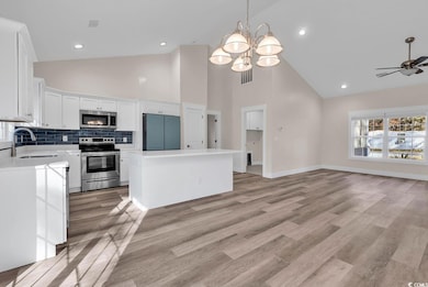 Kitchen featuring decorative light fixtures, stainless steel appliances, decorative backsplash, white cabinetry, and high vaulted ceiling