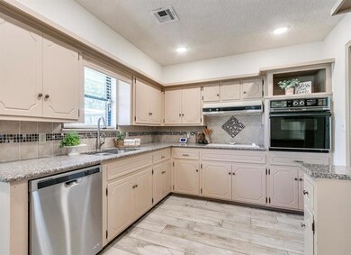 Kitchen featuring light wood-type flooring, backsplash, sink, stainless steel dishwasher, and black oven