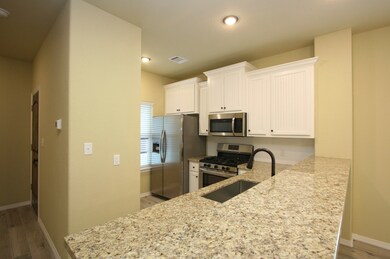 Kitchen has granite counters, stainless appliances (including fridge and gas cook-top), and the same wood-plank tile flooring as the living and dining areas of the home.